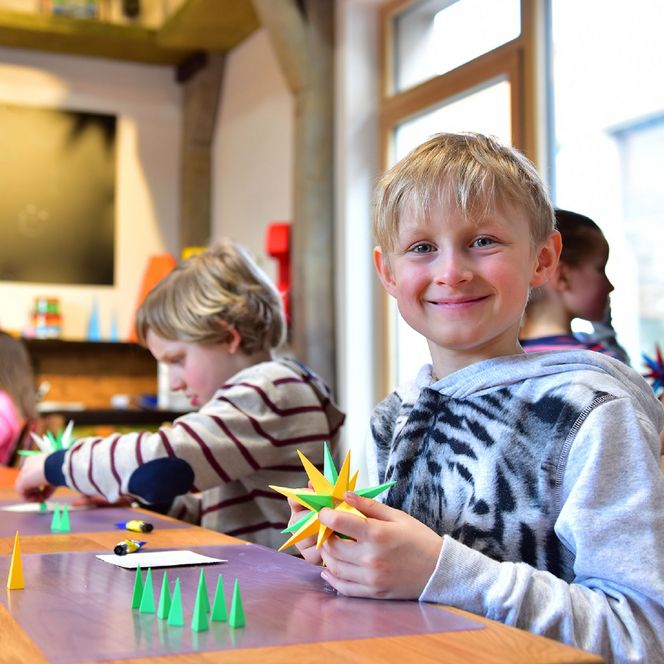 Kinder sitzen an einem Tisch und basteln Herrnhuter Sterne, den bekanntesten Weihnachtsstern aus der Oberlausitz.