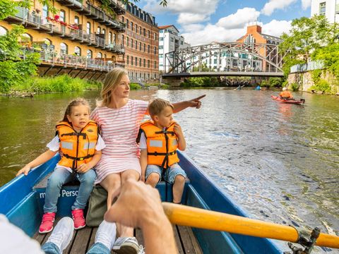 Eine Mutter und zwei Kinder sitzen an der Spitze eines Ruderbootes. Sie fahren über den Kanal in Leipzig.