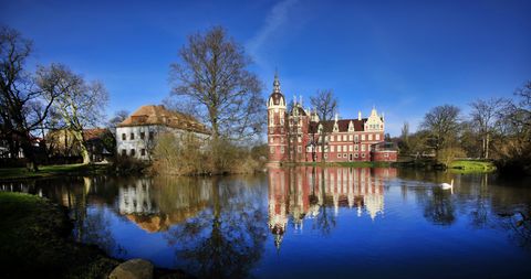 Blick über Wasser zum Schloss das in dunkelroter Fassade erstrahlt