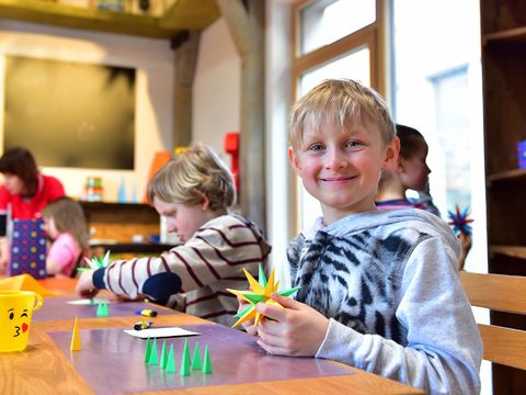 Kinder sitzen an einem Tisch und basteln Herrnhuter Sterne, den bekanntesten Weihnachtsstern aus der Oberlausitz.