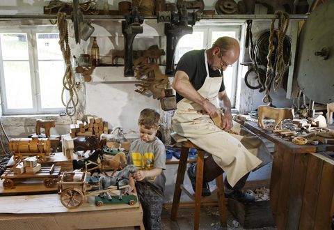 Ein Schnitzer schnitzt an einem Holztier in seiner Werkstatt. In seinem Atelier in Seiffen spielt ein Junge mit einer Pferdefigur. 
