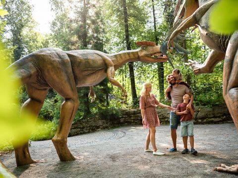 Eine Familie läuft an zwei Dinosauriern vorbei. Sie stehen im Saurierpark.