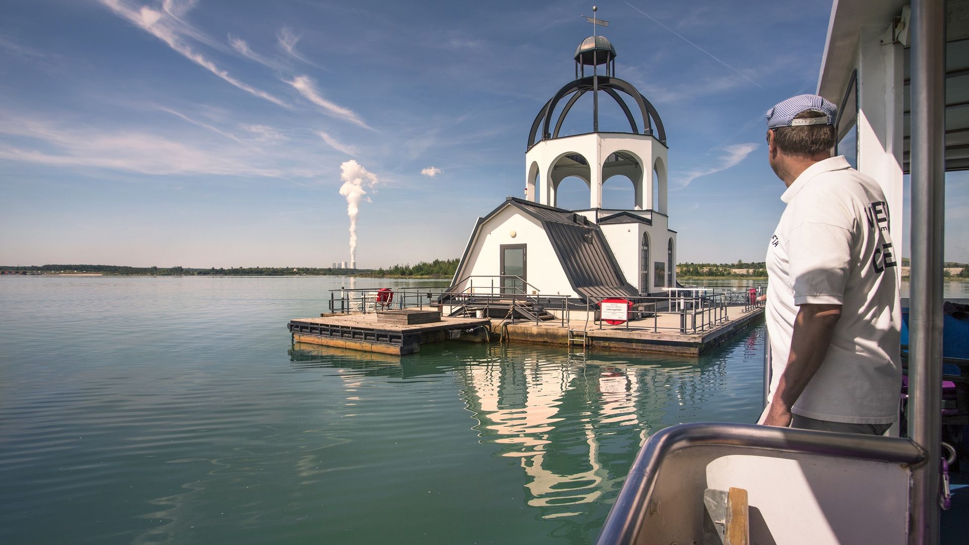 Ein Mann Schaut von einem Schiff aus auf die schwimmende Kirche Vineta. Sie liegt im Leipziger Neuseenland.