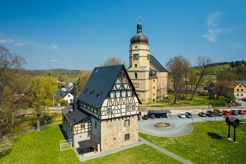 Eine Kirche steht hinter einem Fachwerkhaus, davor ist ein Parkplatz mit Autos.