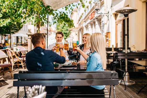 Zwei junge Frauen und zwei junge Männer stoßen miteinander in einem Biergarten an. Sie sind zu Gast in Freiberg. 