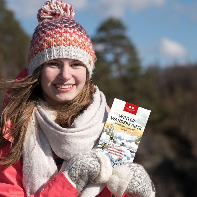Eine Frau geht mit Hilfe der Winterwanderkarte in der Sächsischen Schweiz auf Tour.