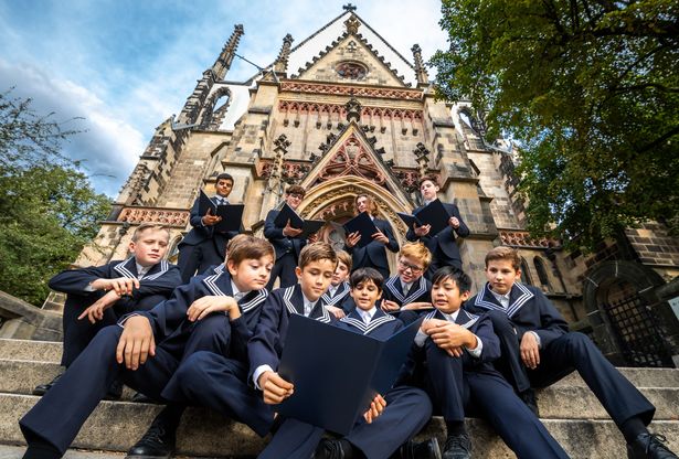 Mehrere Jungen aus dem Thomaner Chor sitzen auf den Stufen vor der Thomaskirche in Leipzig.