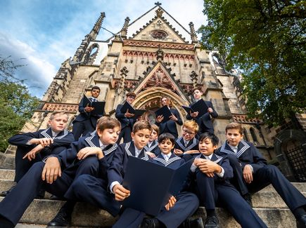 Mehrere Jungen aus dem Thomaner Chor sitzen auf den Stufen vor der Thomaskirche in Leipzig.