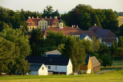 Hinter Häusern und Bäumen steht ein Schloss. Es ist das Barockschloss von Rammenau. 