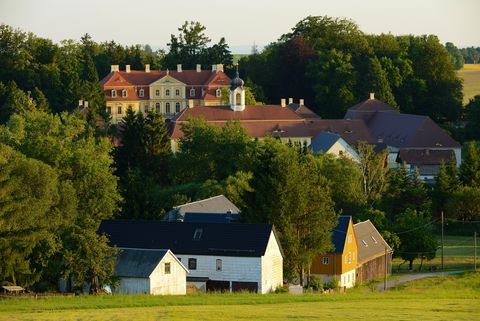 Hinter Häusern und Bäumen steht ein Schloss. Es ist das Barockschloss von Rammenau. 