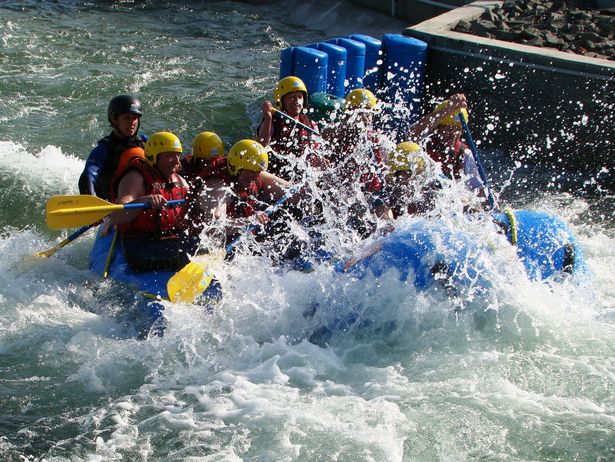 Rafting im Kanupark Markkleeberg. Eine Gruppe sitzt mit Helmen und Paddeln in einem Kanu. Das Wasser um das Boot herum spritzt hoch und trifft die Leute im Boot. 