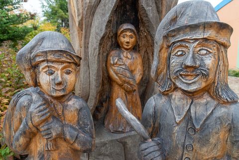 Drei aus Holz geschnitzte Figuren stehen in Schleife. Es sind zwei Männer und eine Frau mit einem Baby im Arm. 