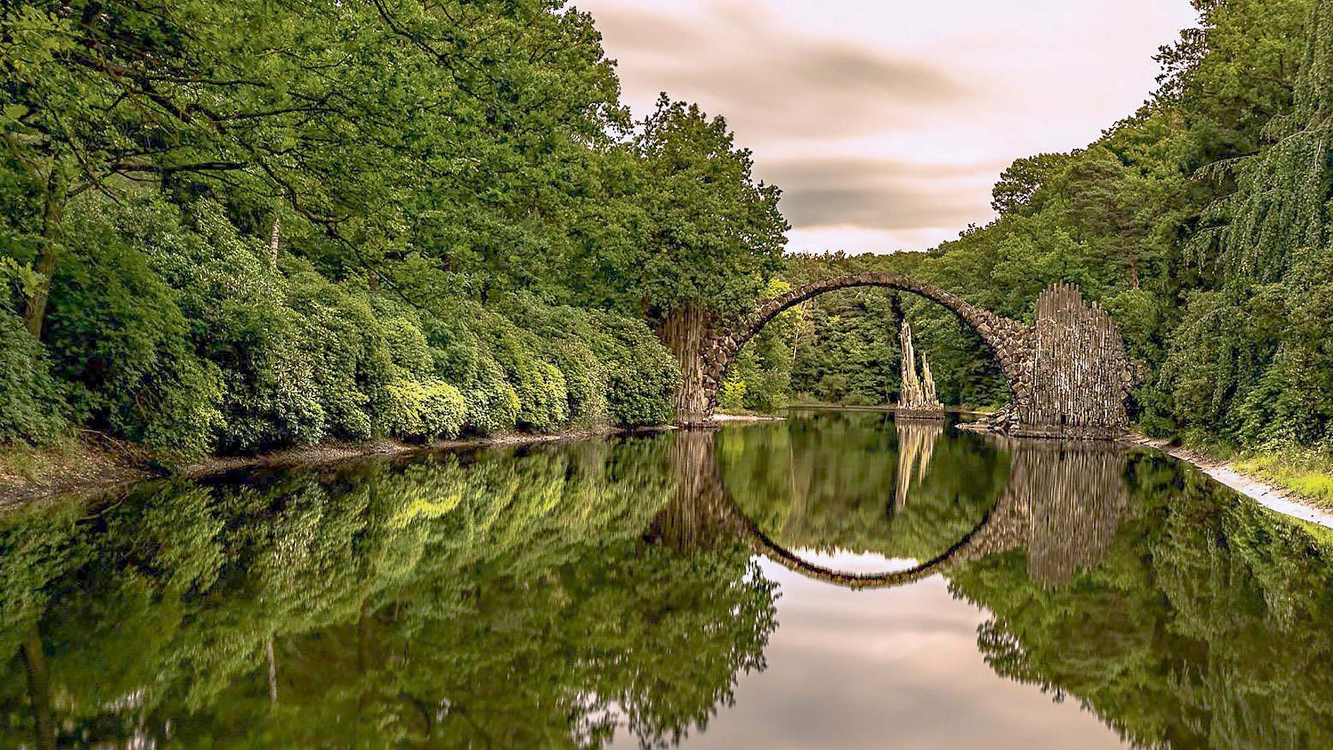 Die Rakotzbrücke spannt sich über einen Teich im Rhododendronpark Kromlau und spiegelt sich im Wasser. 