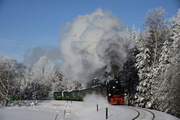 Eine rot-schwarze Dampflok fährt durch schneebedeckte Landschaft.