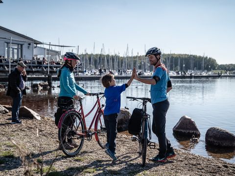 Eine Familie steht mit ihren Rädern am Cospudener See, Vater und Sohn geben sich ein High Five.