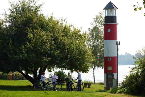 Radfahrer stehen an einem Leuchtturm. Sie machen eine Radtour am Halbendorfer See. 