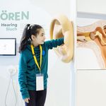 Eine Frau steht im Ausstellungsraum "Hören" des Deutschen Hygienemuseums Dresden. Sie greift mit ihrer linken Hand in ein großes Ohr. Dahinter sieht man die einzelnen Teile.