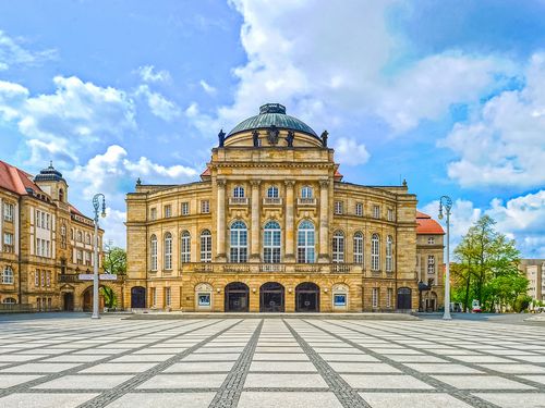 Opernhaus Chemnitz bei Tag mit großer Kuppel und hellem Platz davor. / Chemnitz Opera House in daylight with large dome and open square in front.