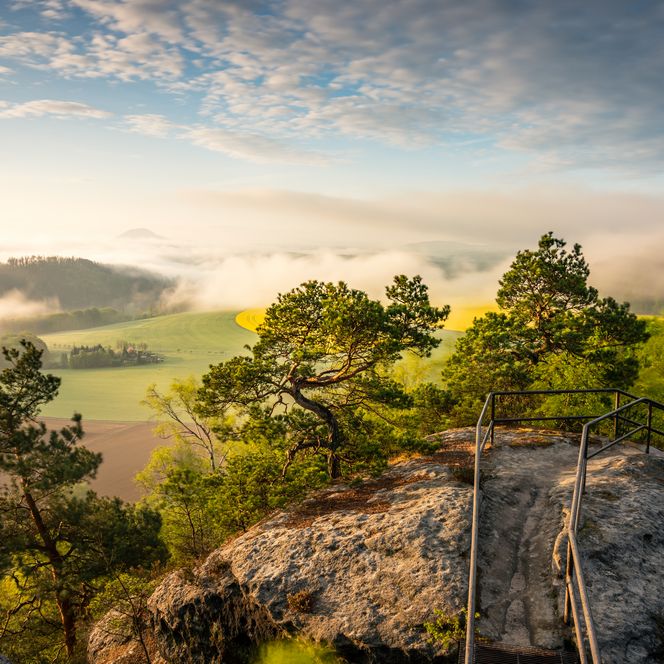 View of a rock in Saxon Switzerland in the midst of trees, a valley and clouds