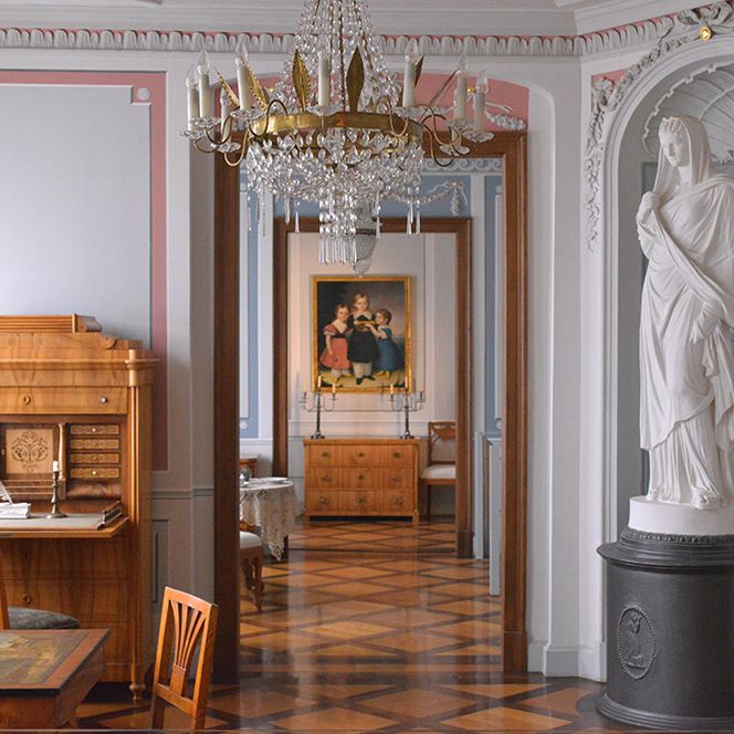 Im Stilzimmer des Vogtlandmuseums steht ein alter Schreibtisch, eine Statue, und ein alter Tisch mit Sofa. 