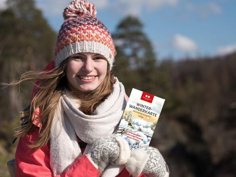 eine Frau geht mit Hilfe der Winterwanderkarte in der Sächsischen Schweiz auf Tour