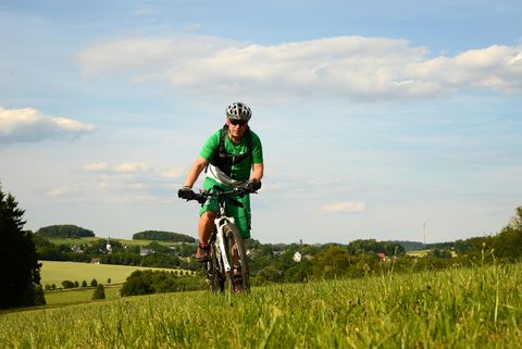 Ein Mountainbiker fährt auf einer Wiese mit seinem Rad. Er ist in der Landschaft bei Jössnitz unterwegs. 