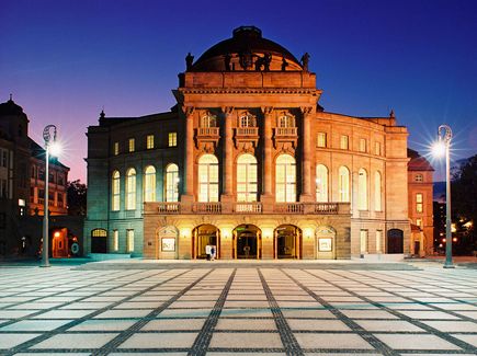 Außenansicht der Oper Chemnitz am Theaterplatz, Gebäudefassade wird beleuchtet, da es dunkel ist