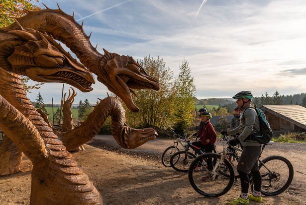 Biker stehen am Wegesrand der Blockline und betrachten Drachenfiguren aus Holz.