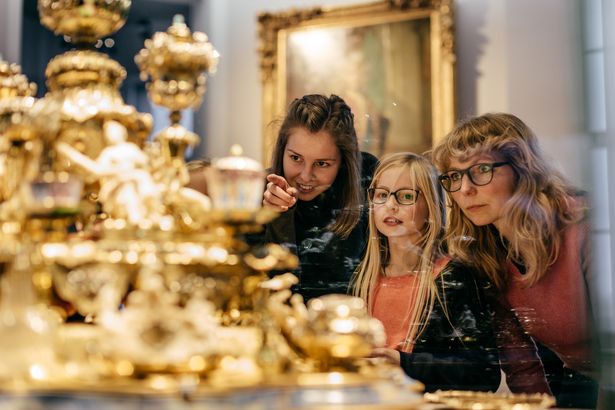 Zwei Frauen und ein Mädchen stehen vor einer Vitrine mit eine goldenen Ausstellungsstück im Residenzschloss Dresden. 