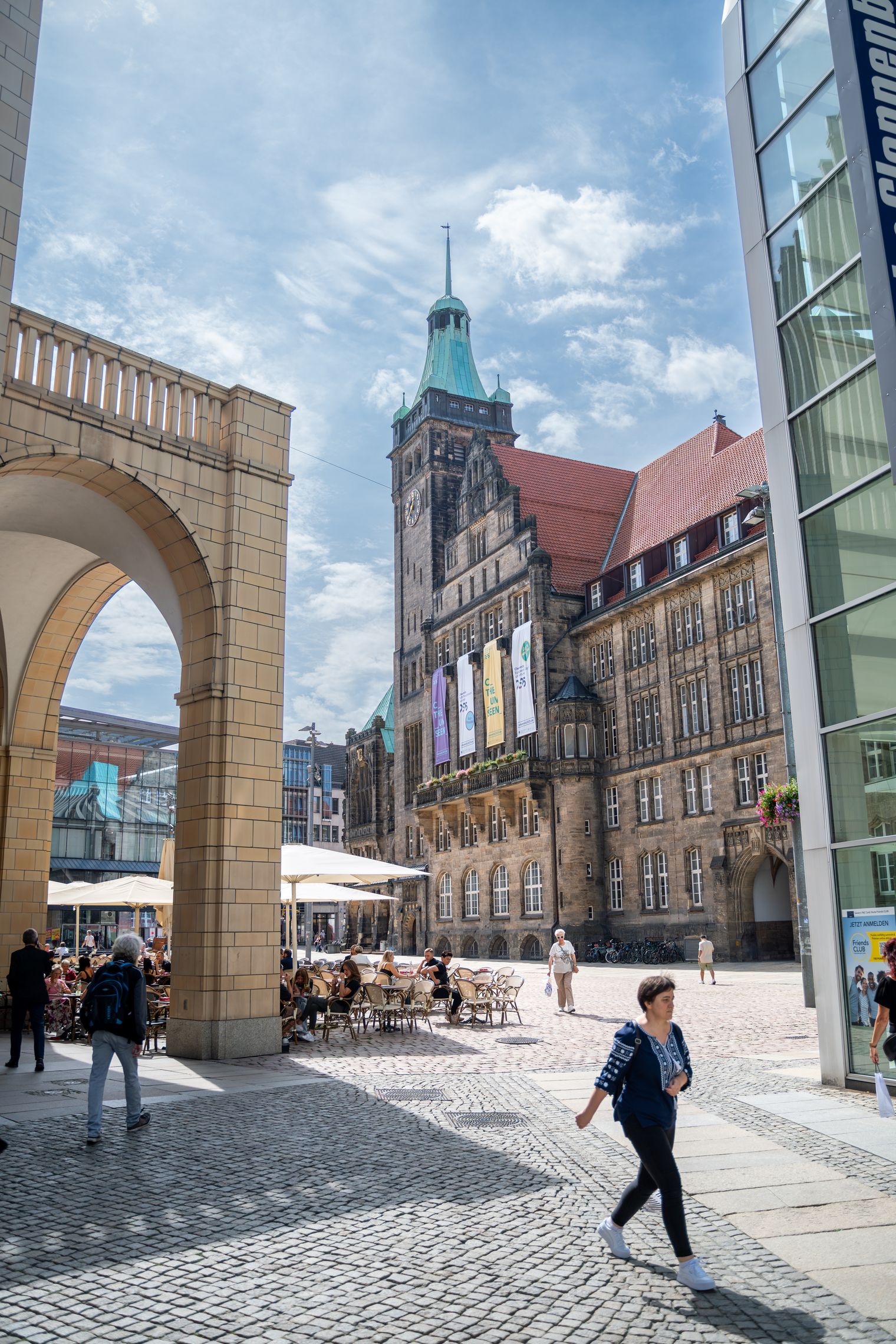 Marktplatz einer größeren Innenstadt gesäumt von historischen und modernen Gebäuden. Ein Mensch läuft uns den gepflasterten Bodenbelag.