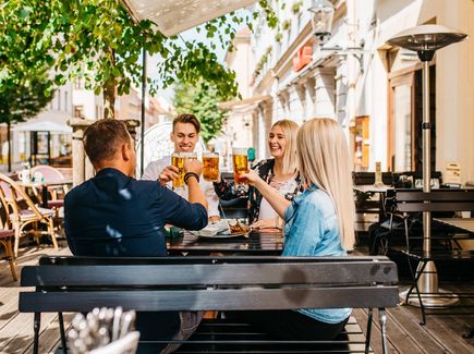 Gruppe sitzt draußen im Biergarten und stoeßt an mit einem Freiberger Bier