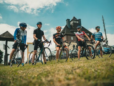 Radfahrer stehen nebeneinander auf einer Wiese, dahinter ein Haus. Sie sind auf der Stoneman-Road unterwegs.