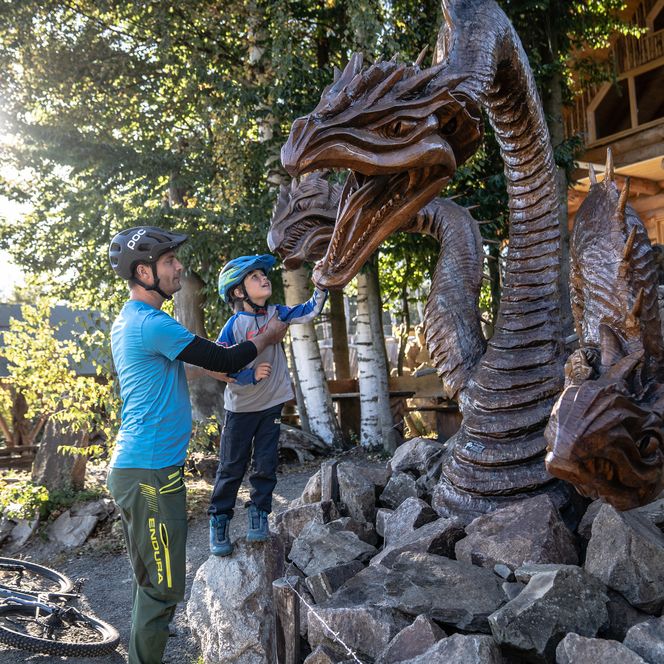 Ein Vater steht mit seinem Sohn vor einem aus Holz gesägten Drachen.