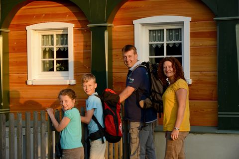 Eine Familie steht an einem Zaun an einem Umgebindehaus. Sie machen einen Dorfspaziergang entlang des Denkmalweges. 