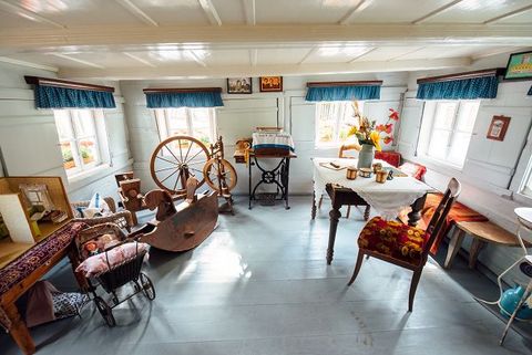 Das Bild zeigt eine Original Lausitzer Blockstube, die als Museum genutzt wird. Das Zimmer ist komplett eingerichtet mit einem gedeckten Tisch und Stühlen, einem Webstuhl, einem Schaukelpferd aus Holz und einem Kinderwagen mit einer Puppe darin.
