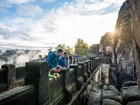 Menschen schauen von der Basteibrücke in der Sächsischen Schweiz herunter in die Landschaft. 