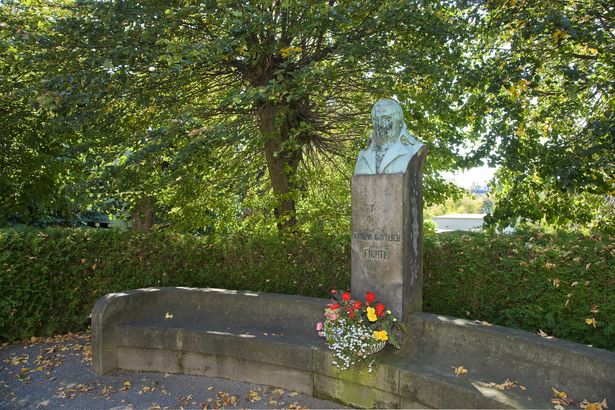 Eine Statue von Johann Gottlieb Fichte steht im Park in Rammenau. Davor stehen Blumen. 