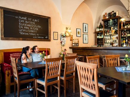 Ein Pärchen sitzt freudestrahlend in einem Restaurant auf einer Couch