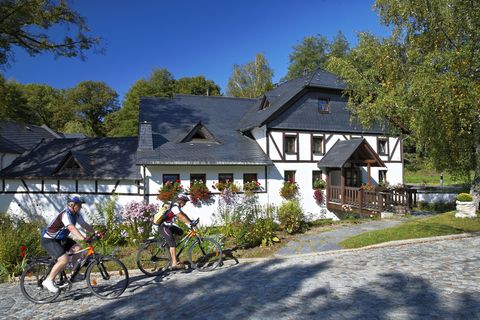 Zwei Radfahrer fahren an der weiß gestrichenen Teichmühle vorbei. 