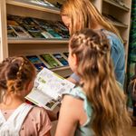 Eine Frau schaut sich mit ihren zwei Töchtern ein Prospekt in der Touristinformation Eibenstock an. Sie stehen vor einem Regal mit weiteren Prospekten und Flyern.