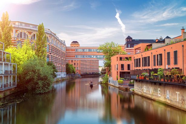 Auf dem Bild ist ein Wasserkanal in Leipzig zu sehen, auf dem ein kleines Boot unterwegs ist. Rechts und links stehen backsteinfarbige Industriegebäude und Bäume, die grünen. Es ist schön Wetter, der Himmel strahlt blau.