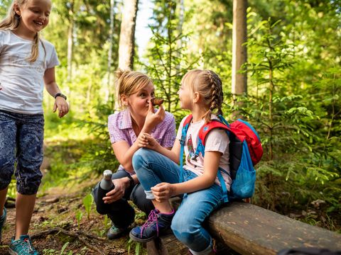 Eine Mutter mit zwei Mädchen geht wandern im Erzgebirge in Eibenstock. Sie machen Pause auf einem Baumstamm. 