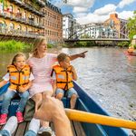 Eine Mutter und zwei Kinder sitzen an der Spitze eines Ruderbootes. Sie fahren über den Kanal in Leipzig.