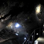 Eine Brücke in der Tiefe der Drachenhöhle Syrau führt über das Wasser. Es ist dunkel, nur einzelne Lichtpunkte leuchten.