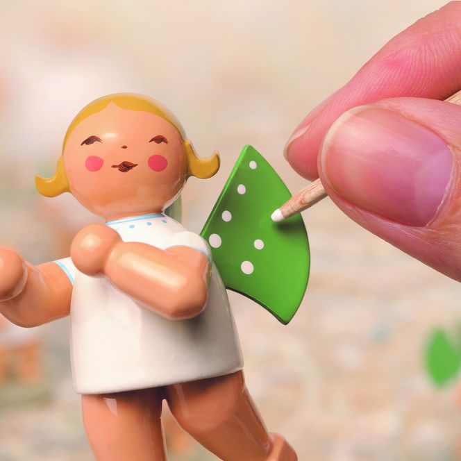 Auf einer kleinen Engelsfigur aus Holz werden die typischen Punkte auf den Flügeln aufgetragen.