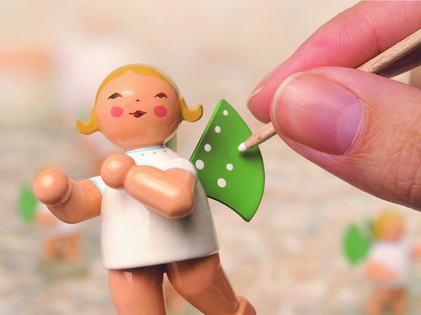 Auf einer kleinen Engelsfigur aus Holz werden die typischen Punkte auf den Flügeln aufgetragen.