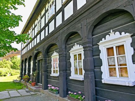 Hausfront eines Hauses mit Bögen aus Holz und Fachwerkbau. Das Bild zeigt die typische Bauweise von Häusern in der Oberlausitz. Vor dem Haus breitet sich ein Garten mit Wiese aus.