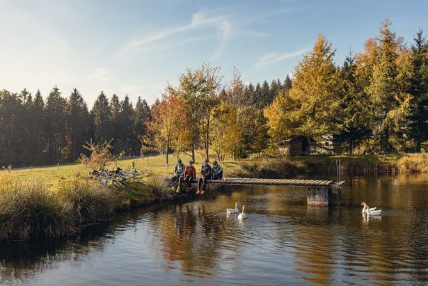 Eine Familie sitzt auf einem Steg am Wasser und hält die Füße ins Wasser. Sie machen eine Pause auf der Blockline-Tour im Erzgebirge.