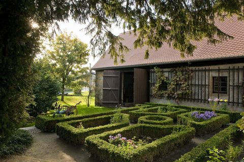 Vor einer offenen Scheune stehen symmetrisch geschnittene Hecken. 