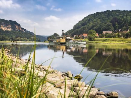 Auf der Elbe fährt ein Schaufelraddampfer. Links und rechts erheben sich die Felsen der Sächsischen Schweiz.